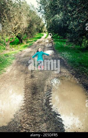 Ragazza in piedi nel mezzo di una strada allagata tra ulivi, Italia Foto Stock