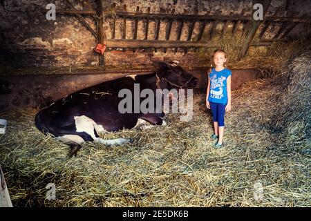 Ragazza in piedi in un fienile accanto a una mucca, Polonia Foto Stock