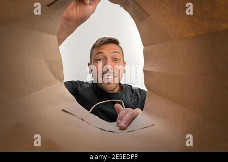 Uomo sorridente felice che guarda nella borsa marrone dello shopping di carta. Foto Stock