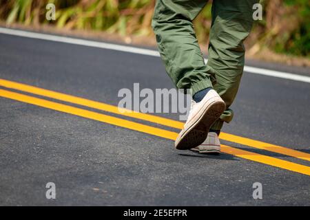 Uomini che indossano sneakers che camminano per le strade con linee gialle. Foto Stock
