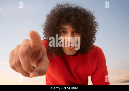 UN GIOVANE CON CAPELLI RICCI CHE PUNTA FELICEMENTE IL DITO VERSO FOTOCAMERA Foto Stock