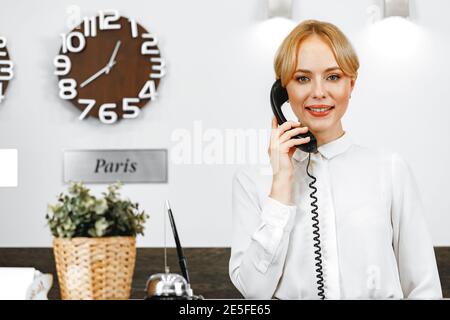 La donna che parla al telefono è un'accogliente addetta alla reception dell'hotel Foto Stock
