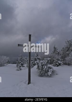 Croce religiosa in legno sulla cima del picco di Schliffkopf nelle colline della Foresta Nera, Germania in neve profonda con alberi di conifere ghiacciati in giornata nuvolosa. Foto Stock