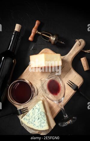 Degustazione di vini e formaggi, sparati dall'alto su sfondo nero, con cavatappi vintage e una bottiglia Foto Stock