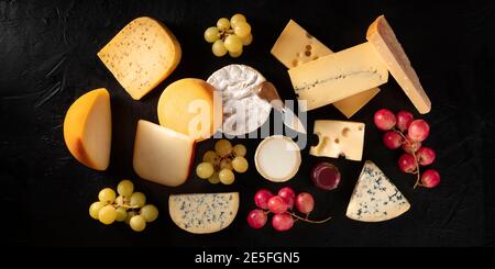 Panorama del formaggio, molti tipi diversi di formaggi, sparati dall'alto su uno sfondo scuro con uva Foto Stock