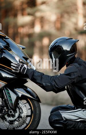 Il conducente della motocicletta con tuta in pelle e casco si siede davanti del motociclo da solo e mettere le sue mani sul fari Foto Stock