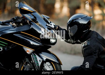 Il conducente della motocicletta con tuta in pelle e casco si siede davanti del motociclo da solo e mettere le sue mani sul fari Foto Stock