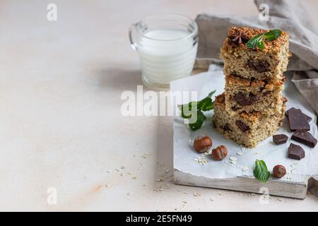 Quadrati di farinata d'avena con cioccolato e una tazza di latte, fondo di cemento chiaro. Dieta bar. Panetteria sana per colazione o dessert. Messa a fuoco selettiva. Foto Stock