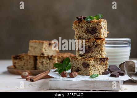 Quadrati di farinata d'avena con cioccolato e una tazza di latte, fondo di cemento chiaro. Dieta bar. Panetteria sana per colazione o dessert. Messa a fuoco selettiva. Foto Stock