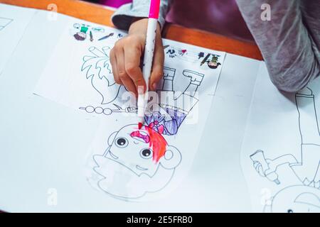 Le mani di bambina ragazzina, disegnando pagine di carta da colorare con la penna di punta di feltro rosa. Felice infanzia, casa e scuola materna, immaginazione Foto Stock