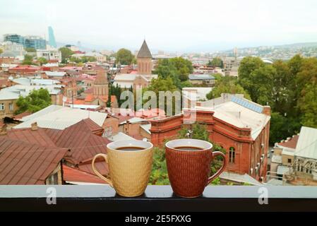 Coppia di tazze di caffè calde sul balcone che ringhiera con Vista aerea di Tbilisi in background Foto Stock