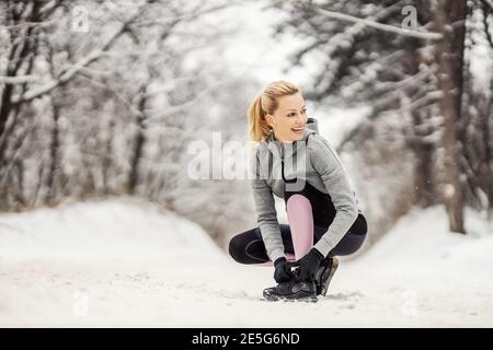 Donna sportiva che lega la scarpa mentre si inginocchiava su un percorso innevato durante il giorno d'inverno. Abbigliamento sportivo, stile di vita sano, fitness invernale Foto Stock