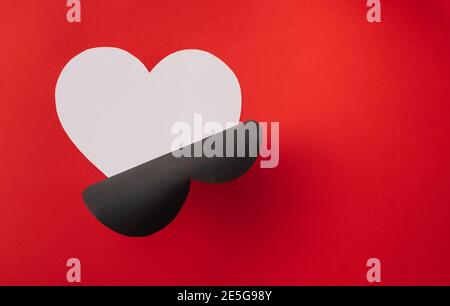 Forma a cuore nero tagliata e sbucciata per rivelare il bianco simbolo del profilo d'amore su sfondo di carta rosso Foto Stock