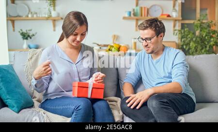 Ordinazione di regali online. Un uomo dà a una donna un regalo che ha ordinato attraverso il luogo, un deposito in linea. La ragazza prende fuori un regalo rosso da un cartone Foto Stock