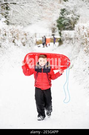 Un ragazzo va a casa dopo aver slittato nel Gloucestershire Cotswolds, Regno Unito Foto Stock