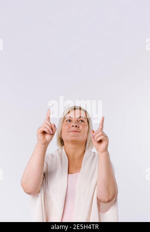 Una donna anziana guarda in su e punta le sue dita di indice in su allo spazio vuoto bianco. Foto Stock