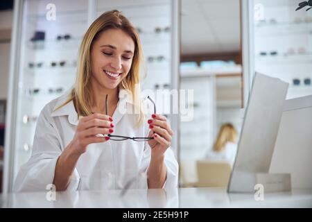 Felice donna allegra che guarda alle nuove lenti in vetro mentre si passa il tempo in ambulatorio di oftalmologia Foto Stock