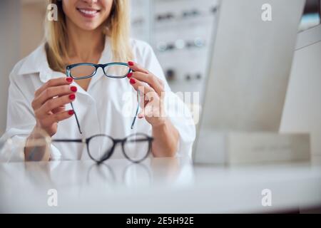 Elegante donna di charme in bluse bianche che sceglie nuovi obiettivi per occhiali in clinica oftalmologica Foto Stock