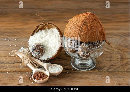 Concetto di cibo sano. Palline di energia di cocco fatte in casa in guscio di cocnut su sfondo di legno Foto Stock