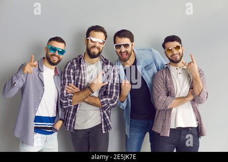 Gruppo di giovani uomini in occhiali da sole guardando la macchina fotografica, facendo il gesto del corno e divertendosi Foto Stock