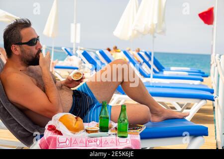 Due amici maschi seduti sulle panchine stanno mangiando sopra il molo insieme mentre godendo la loro vacanza Foto Stock