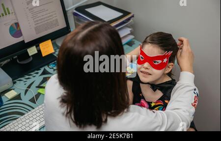 Donna telelavoro e mettere maschera costume su sua figlia Foto Stock