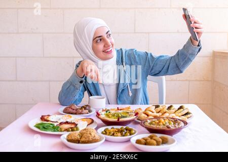 La ragazza musulmana sta mangiando la prima colazione e chiamando i suoi amici Foto Stock