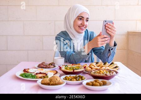 La ragazza musulmana sta mangiando la prima colazione e chiamando i suoi amici Foto Stock