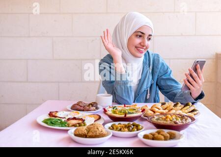 La ragazza musulmana sta mangiando la prima colazione e chiamando i suoi amici Foto Stock