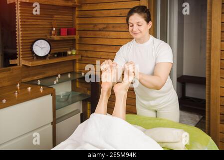 Donna massaggiatrice che fa massaggio tradizionale del piede. Bellissimo modello godendo di un trattamento in un centro termale Foto Stock