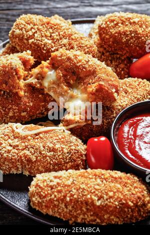 Suppli al telefono fast food italiano - crocchette di riso fritto farcite con mozzarella servite su un piatto nero con gambi di sedano, pomodori e ketchup Foto Stock