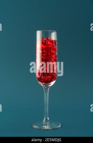Bella card con bicchiere di champagne riempito con cuori rossi trasparenti su sfondo di aqua scuro. Concetto di amore e celebrazione. Design perfetto per qualsiasi tipo di purpo Foto Stock