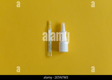 Gocce nasali, termometro, vari farmaci giacciono sul tavolo, vista dall'alto, su sfondo giallo, FlatLay Foto Stock