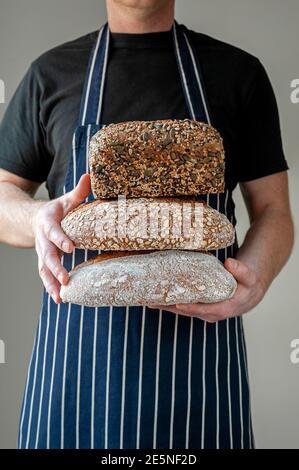 Primo piano alle mani dei fornai che tengono davanti a lui una selezione di loafs organici di pane di pasta acida. Foto Stock