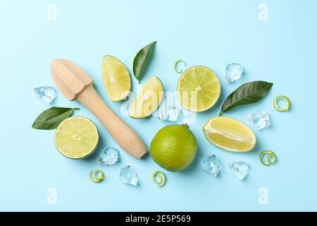 Piatto con lime, centrifuga in legno, ghiaccio, buccia e foglie su sfondo blu Foto Stock