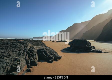 Formazione vulcanica di roccia nera sulla spiaggia di sabbia. Pietre quadrate sulla costa. Portogallo, costa dell'Algarve. Foto Stock