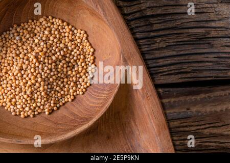 Primo piano di semi di senape/Rai o semi di senape bruno in un piccolo piatto su sfondo di legno Foto Stock