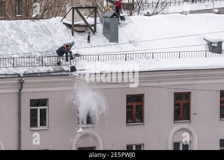 Team di lavoratori di sesso maschile pulire il tetto dell'edificio da neve con pale in cinghie di fissaggio del mantra Foto Stock