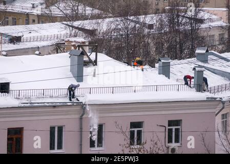 Team di lavoratori di sesso maschile pulire il tetto dell'edificio da neve con pale in cinghie di fissaggio del mantra Foto Stock