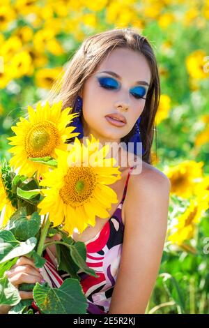 Ritratto di una giovane bella ragazza con trucco luminoso dentro un campo di girasole Foto Stock