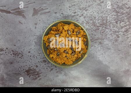 Vista dall'alto di una ciotola piena di fiocchi di crusca e uvetta, cereali per la colazione su sfondo grigio. Foto Stock