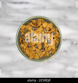 Vista dall'alto di una ciotola piena di fiocchi di crusca e uvetta per la colazione, cereali su sfondo di marmo grigio. Foto Stock