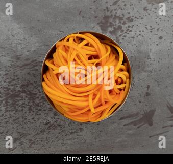 Vista dall'alto di una ciotola in metallo contenente una porzione di tagliatelle di zucca su sfondo grigio. Foto Stock