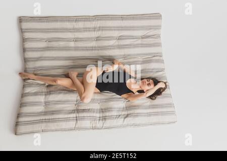 Chill. Vista dall'alto bella giovane donna sullo sfondo del materasso a righe. Divertimento, felice, a tutta lunghezza. Ballare, ottenere l'umore pazzo, posa elegante. Indossa la ragazza con il costume da bagno sportivo nero. CopySpace. Foto Stock