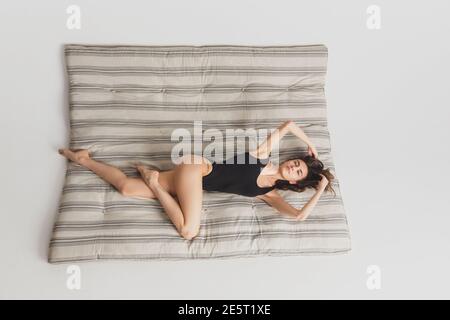 Chill. Vista dall'alto bella giovane donna sullo sfondo del materasso a righe. Divertimento, felice, a tutta lunghezza. Ballare, ottenere l'umore pazzo, posa elegante. Indossa la ragazza con il costume da bagno sportivo nero. CopySpace. Foto Stock