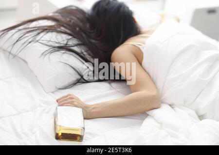 Donne sdraiate in letto bianco con una bottiglia di whisky mano Foto Stock