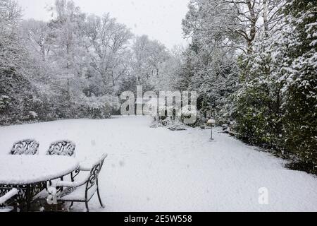 Tavoli e sedie all'aperto su un patio e alberi coperti di neve durante una nevicata pesante in un giardino suburbano Woking, Surrey, Inghilterra sud-orientale Foto Stock