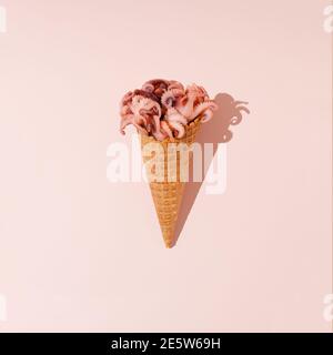 Layout creativo realizzato con polpi rosa freschi e coni gelato su morbido sfondo rosa pastello. Pesce estate concetto minimo. Foto Stock