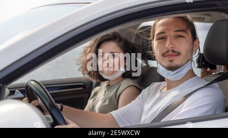 I giovani che indossano una maschera protettiva per il viso sono seduti sui sedili anteriori del passeggero e guardano la telecamera. Virus corona pandemic Concept.viaggio su strada Foto Stock