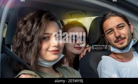 I giovani amici che indossano una maschera protettiva che guarda la fotocamera sono seduti in auto. Concetto pandemico del virus corona. Viaggio su strada in nuova normalità. Foto Stock